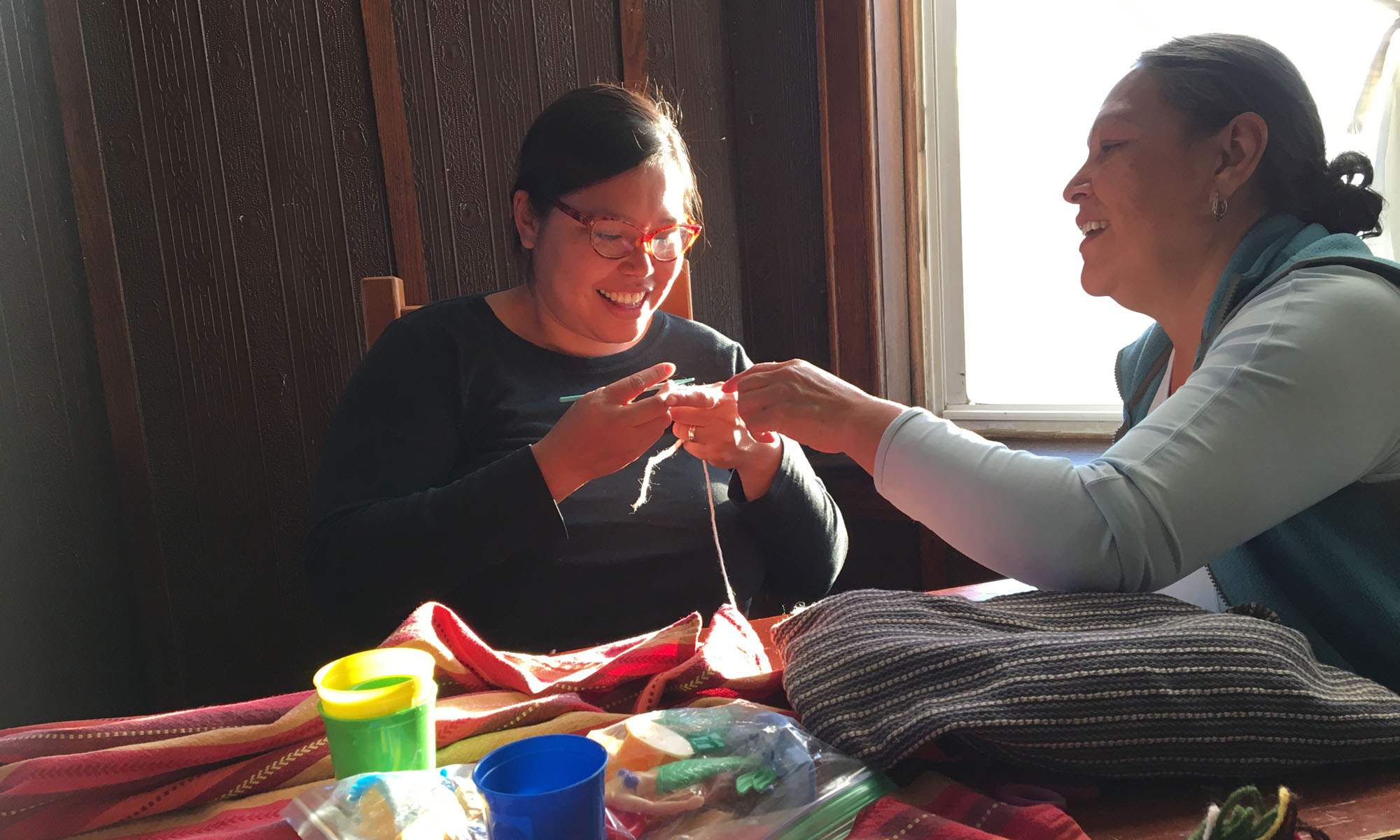 Rosa and her Mami sit at a table crocheting.